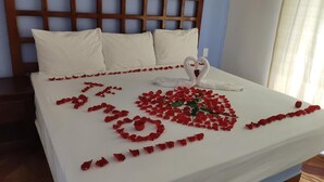 Een net opgemaakt bed met witte lakens, een houten hoofdbord en rozenblaadjes in de vorm van een hart op het beddegoed.