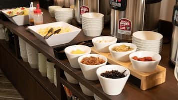 A buffet setup with various food items in bowls and plates, a coffee machine, and stacked plates.