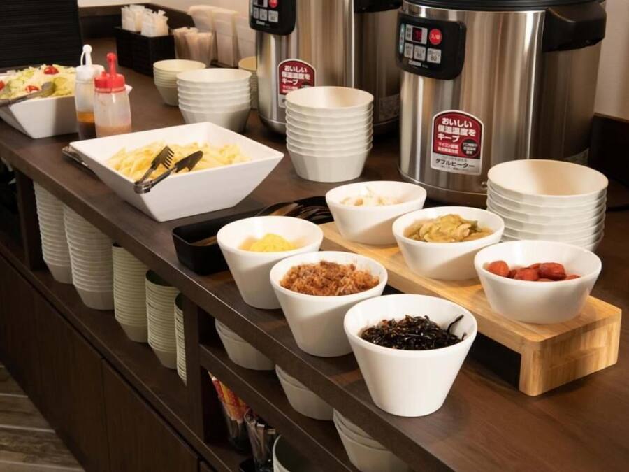 A buffet setup with various food items in bowls and plates, a coffee machine, and stacked plates.