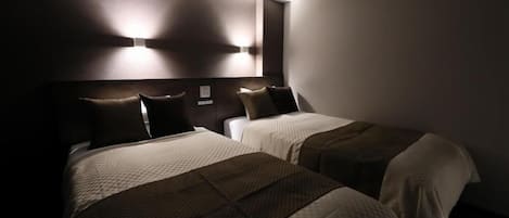 Et hotelværelse med to senge, en mørk sengegavl og en lampe monteret på væggen.