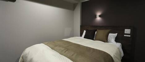 A hotel room with a large bed, a dark headboard, and a wall-mounted light fixture.