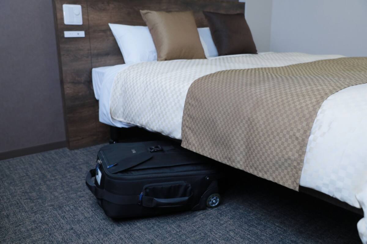 Una habitación de hotel con cama, cabecera, maleta y suelo alfombrado.