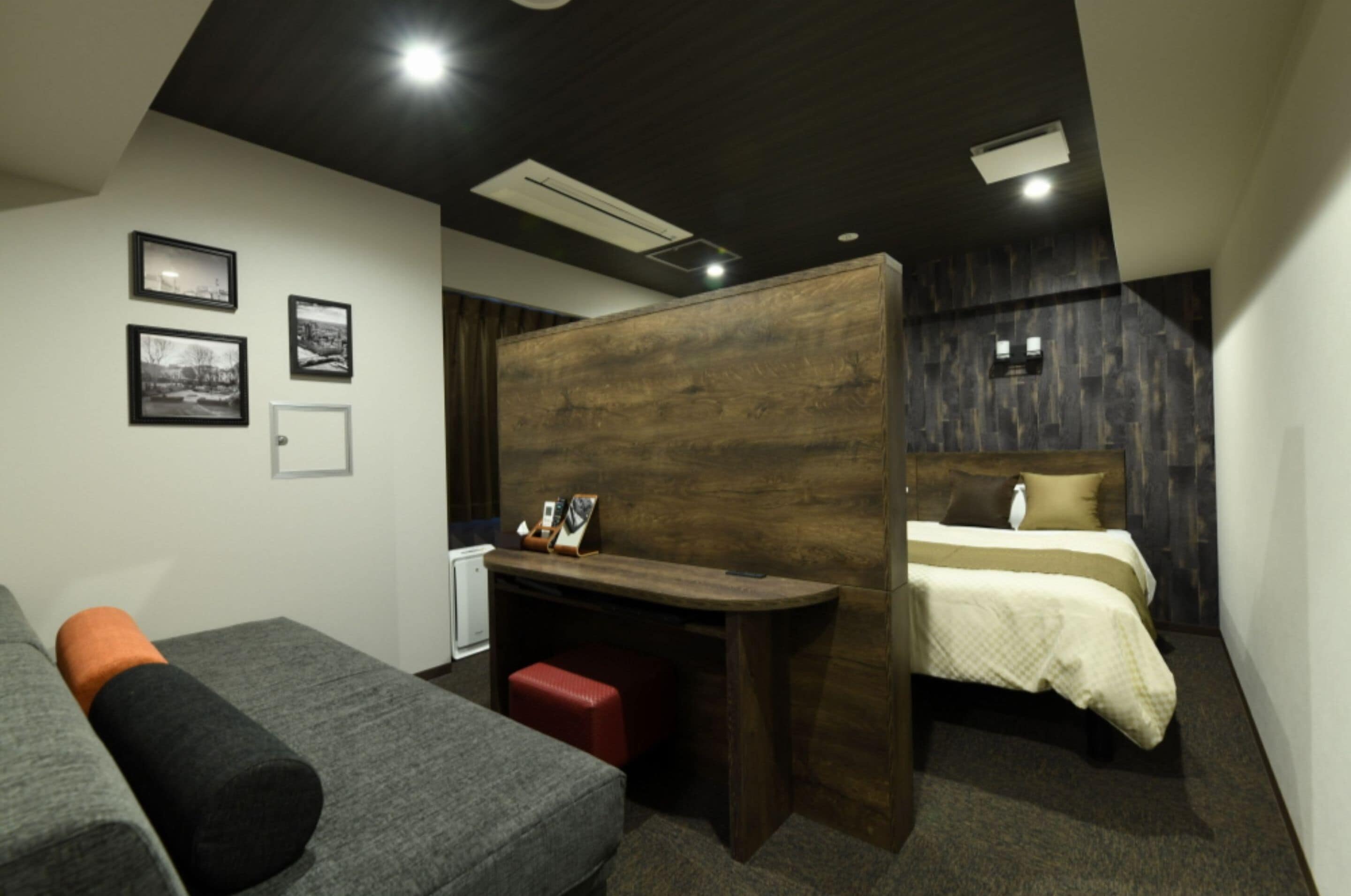 A compact hotel room with a bed, a desk, and a sofa. There are three framed pictures on the wall.