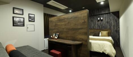 A compact hotel room with a bed, a desk, and a sofa. There are three framed pictures on the wall.
