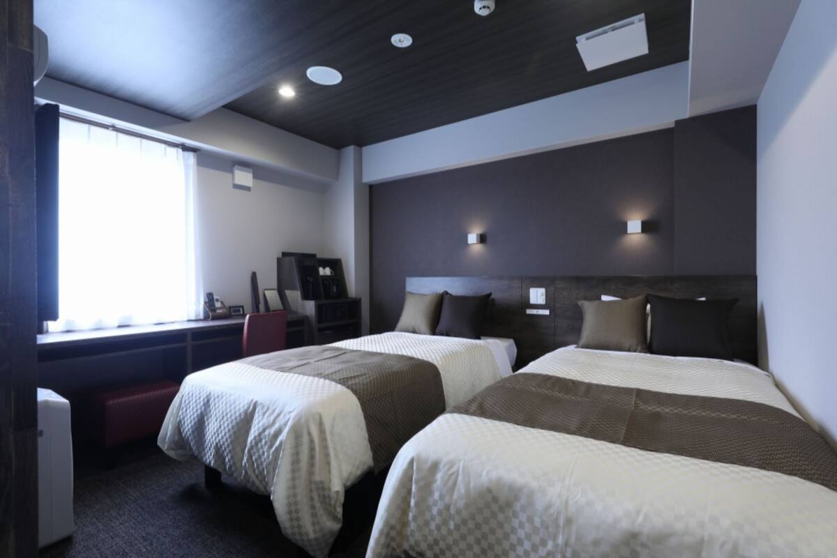 Una habitación de hotel con dos camas, un escritorio y una ventana.