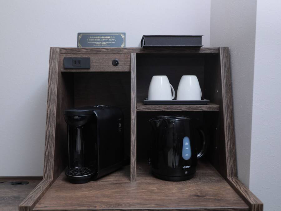 Een houten kastje met een koffiezetapparaat, een waterkoker en twee witte kopjes.