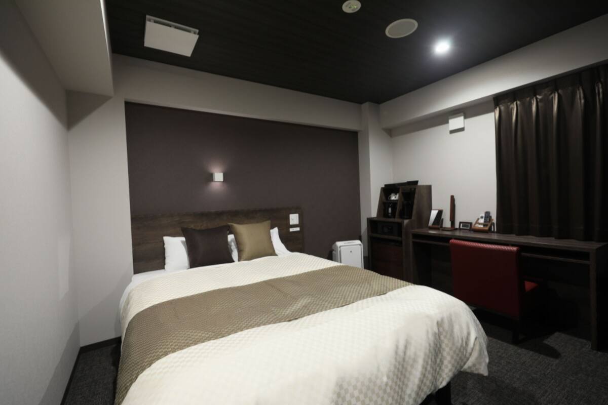 Una habitación de hotel con cama, escritorio, silla, armario y espejo.
