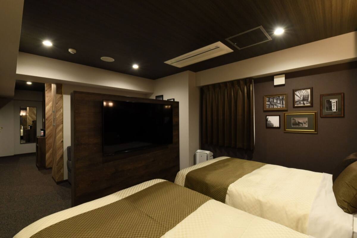 Habitación de hotel con dos camas, un televisor de pantalla plana grande, un revestimiento de pared de madera y fotografías enmarcadas.