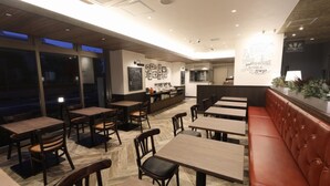 Ein Restaurantinneres mit Holztischen und -stühlen, einer rot gepolsterten Bank und einer Bäckertheke.