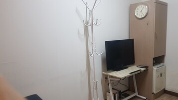 A room with a desk, a television, a coat rack, and a clock on the wall.