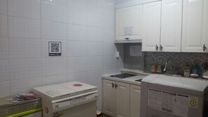 A small kitchenette with white cabinets, a microwave, and a sink. There is a QR code on the wall and a small trash bin. - Jukjeon Guesthouse iwantlivingtel (Yongin)