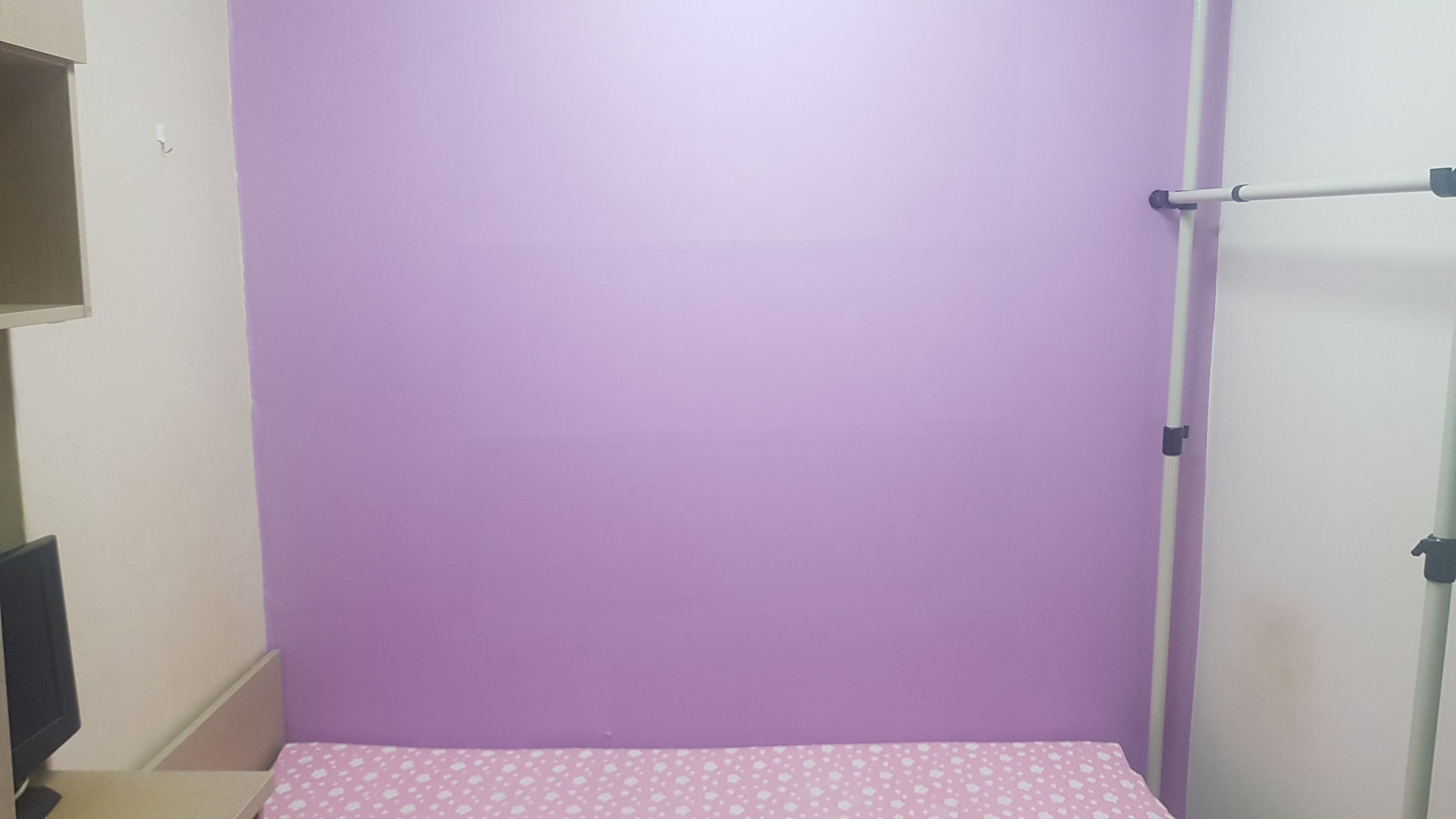 Una habitación con una pared morada, una cama con edredón rosa con lunares y una puerta blanca con picaporte.