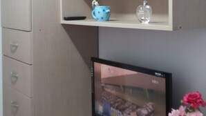 A room with a beige desk, a computer monitor, a vase with flowers, and a cabinet with drawers. - Jukjeon Guesthouse iwantlivingtel (Yongin)