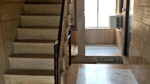 A staircase with a wooden handrail and marble steps leading to a landing with a window and a radiator.