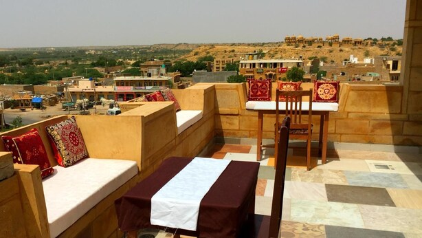 A rooftop terrace with seating and tables, offering a view of a cityscape and distant hills.