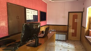 A reception desk with a computer, a telephone, and a bulletin board with information. There is a door with a sign, a bench, and a patterned floor.