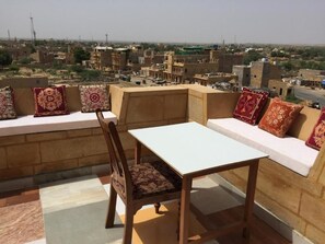 A corner seating area with a table and a chair, a sofa with patterned cushions, and a view of a cityscape.