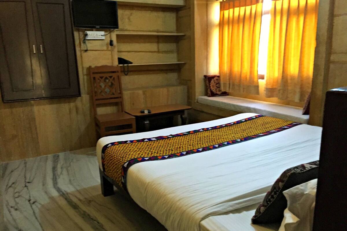 A hotel room with a bed, a desk, a chair, a TV, and a window with curtains.