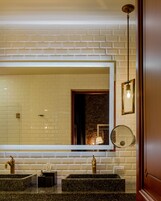 Un baño con un espejo grande, un lavabo con grifo dorado y una lámpara sobre el espejo.