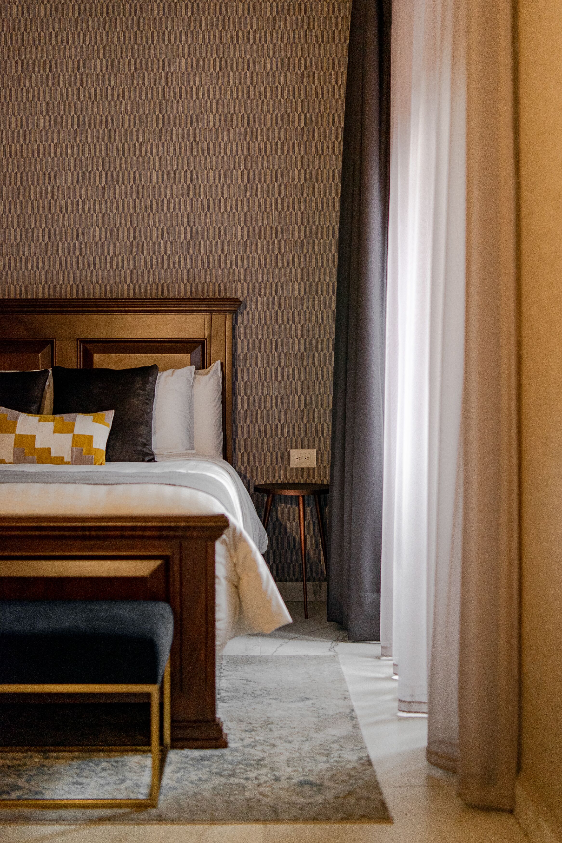 Una habitación de hotel con una cama grande, cabecero de madera, una mesita de noche y un banco.