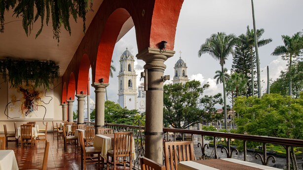 A restaurant with wooden chairs and tables, a red archway, and a view of two church towers. - Hotel Boutique Casa Zevallos (Córdoba)