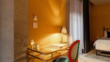 Una habitación de hotel con escritorio de vidrio, una silla, una cama y una mesita de noche.