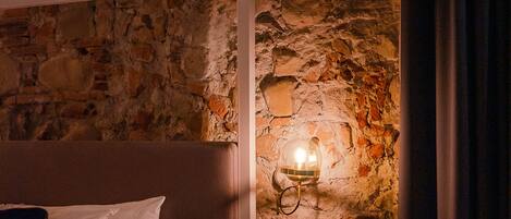 Un dormitorio con pared de piedra, una cama con ropa de cama blanca y una mesita de noche.