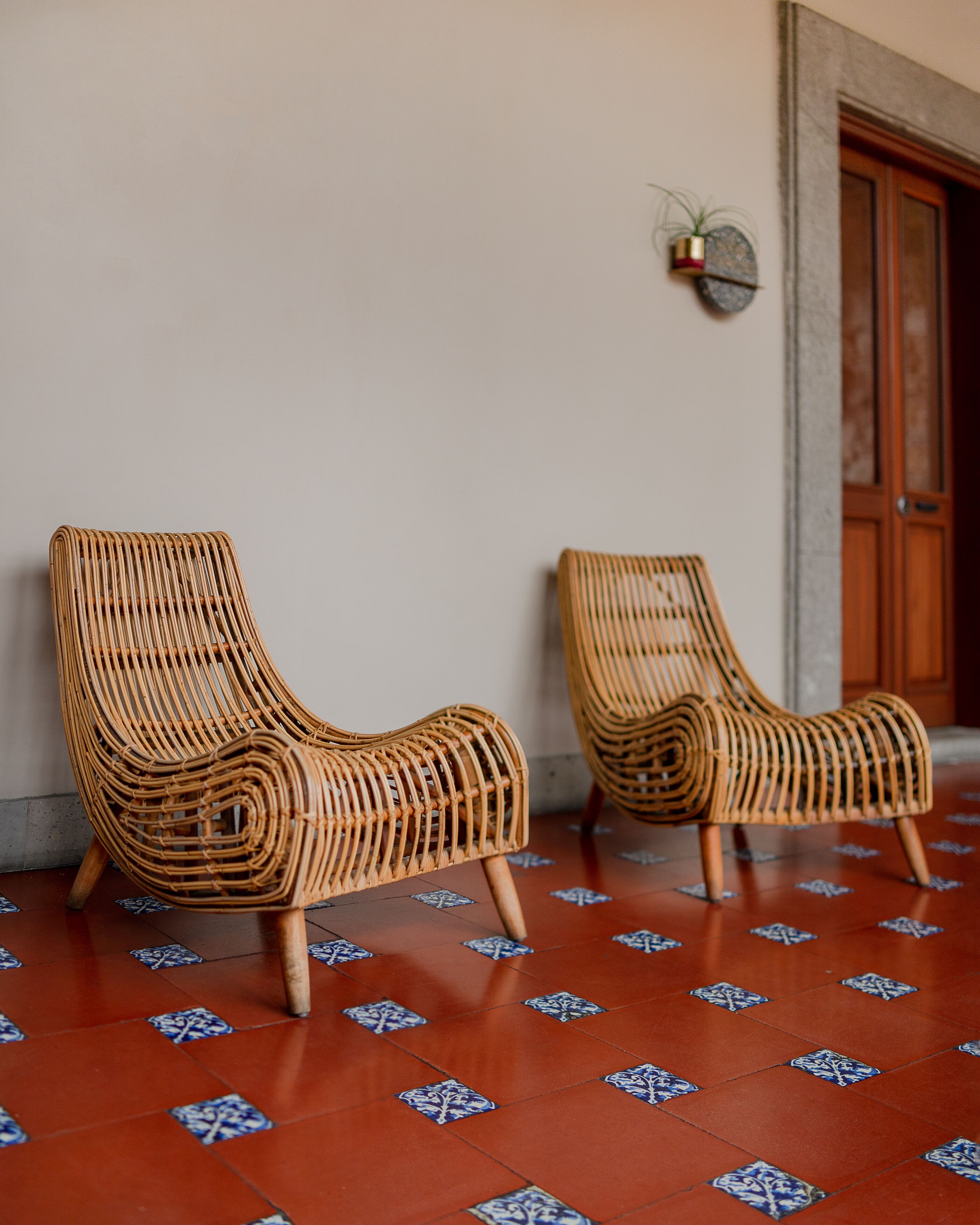 Two wicker lounge chairs with wooden legs, positioned on a tiled floor with a geometric pattern.
