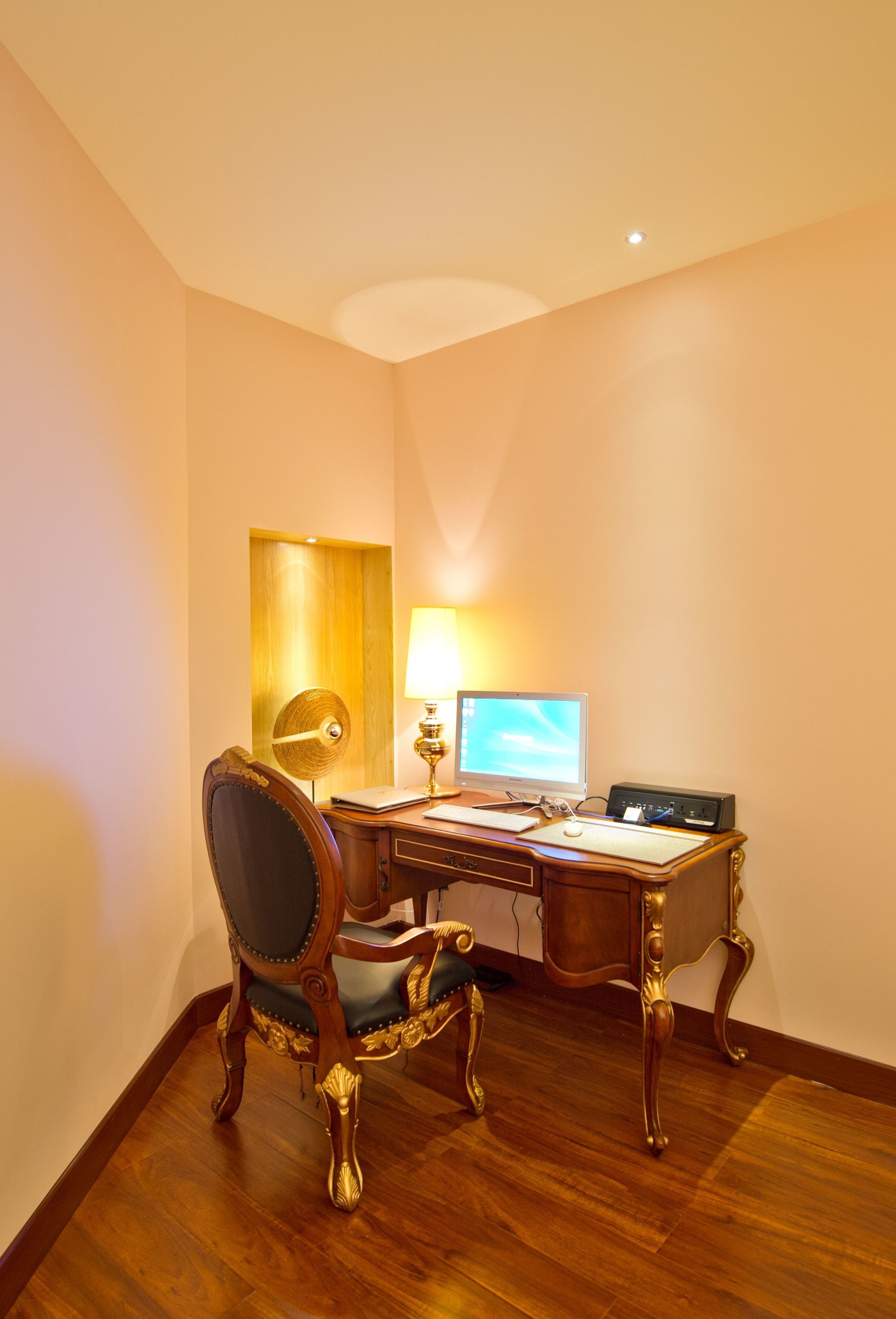 Une pièce d’angle avec un bureau en bois, deux chaises, un ordinateur et une lampe.