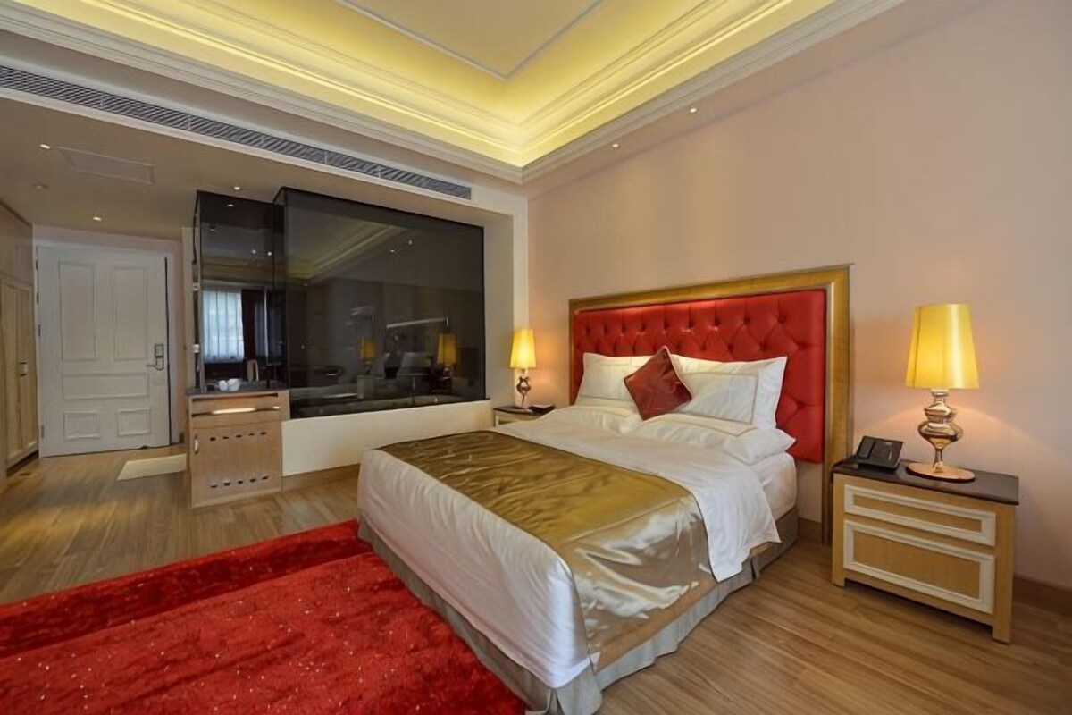 Une chambre d’hôtel avec un grand lit, des tables de chevet, une moquette rouge et une grande fenêtre.