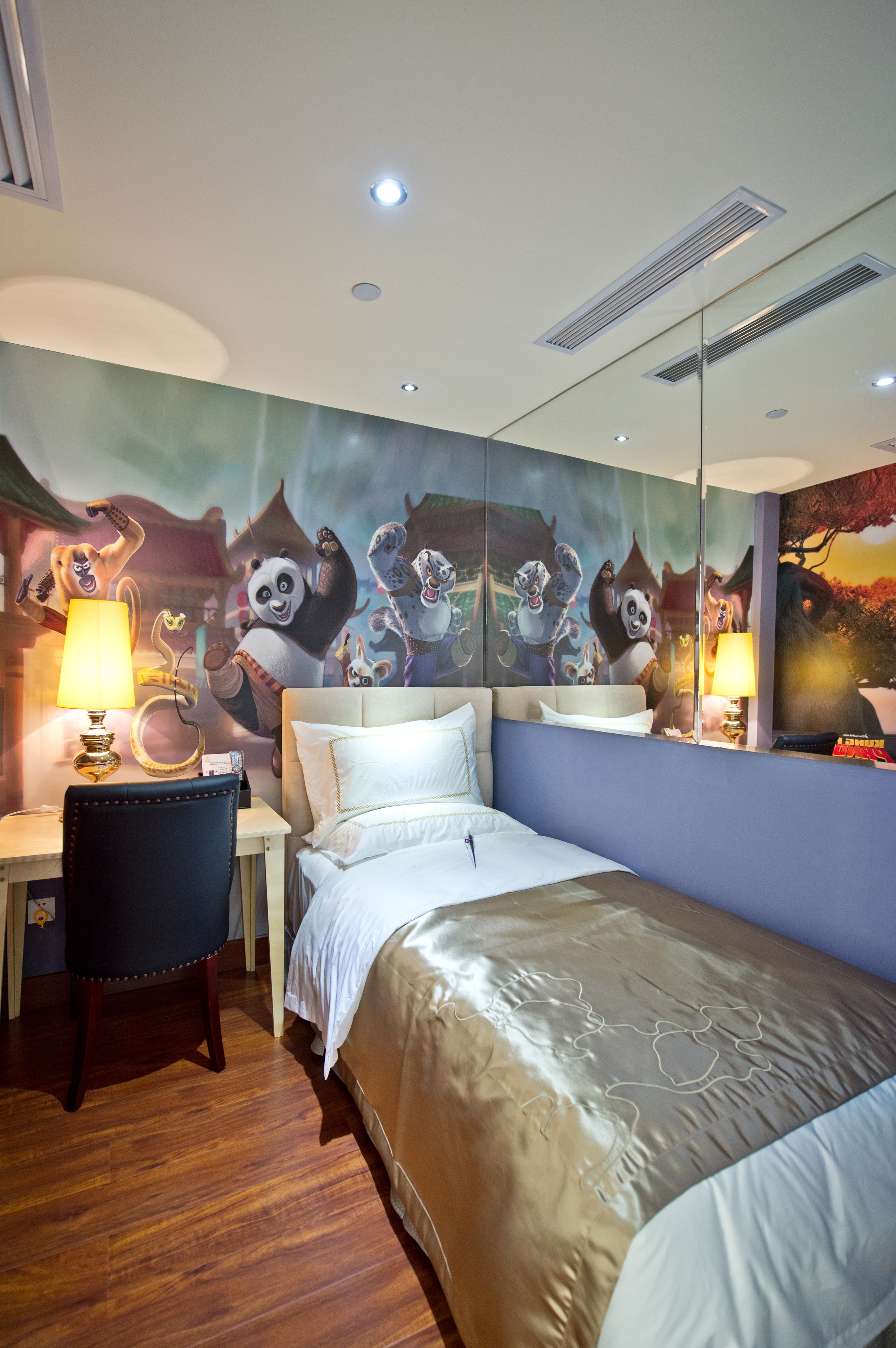 Habitación de hotel con cama, escritorio y silla. En la pared, un mural con personajes animados.