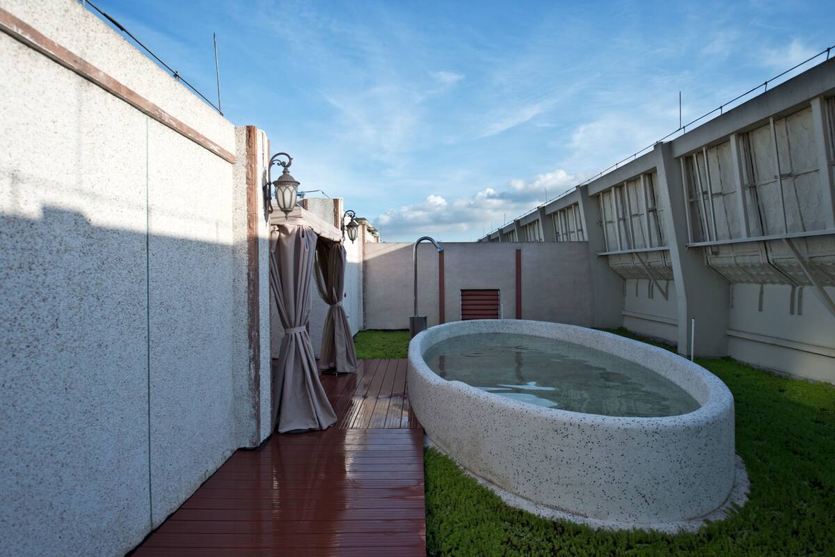 A courtyard with a swimming pool, a wooden deck, and a covered seating area.