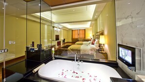 Una habitación de hotel con una bañera grande, una cama con televisor y un espejo que refleja la habitación.