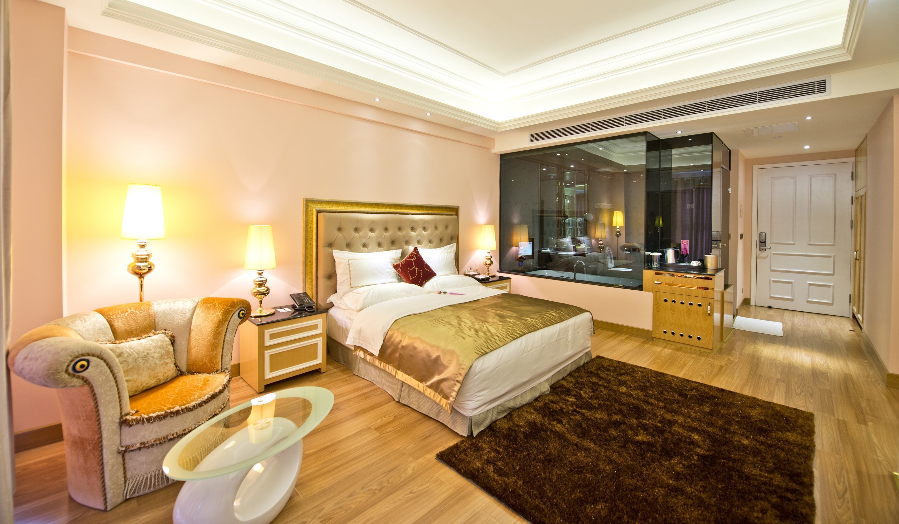 A hotel room with a large bed, a sitting area with a chair and table, a large mirror, and a wardrobe.