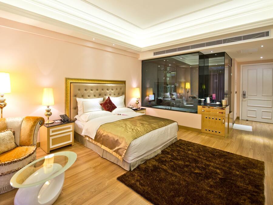 A hotel room with a large bed, a sitting area with a chair and table, a large mirror, and a wardrobe.