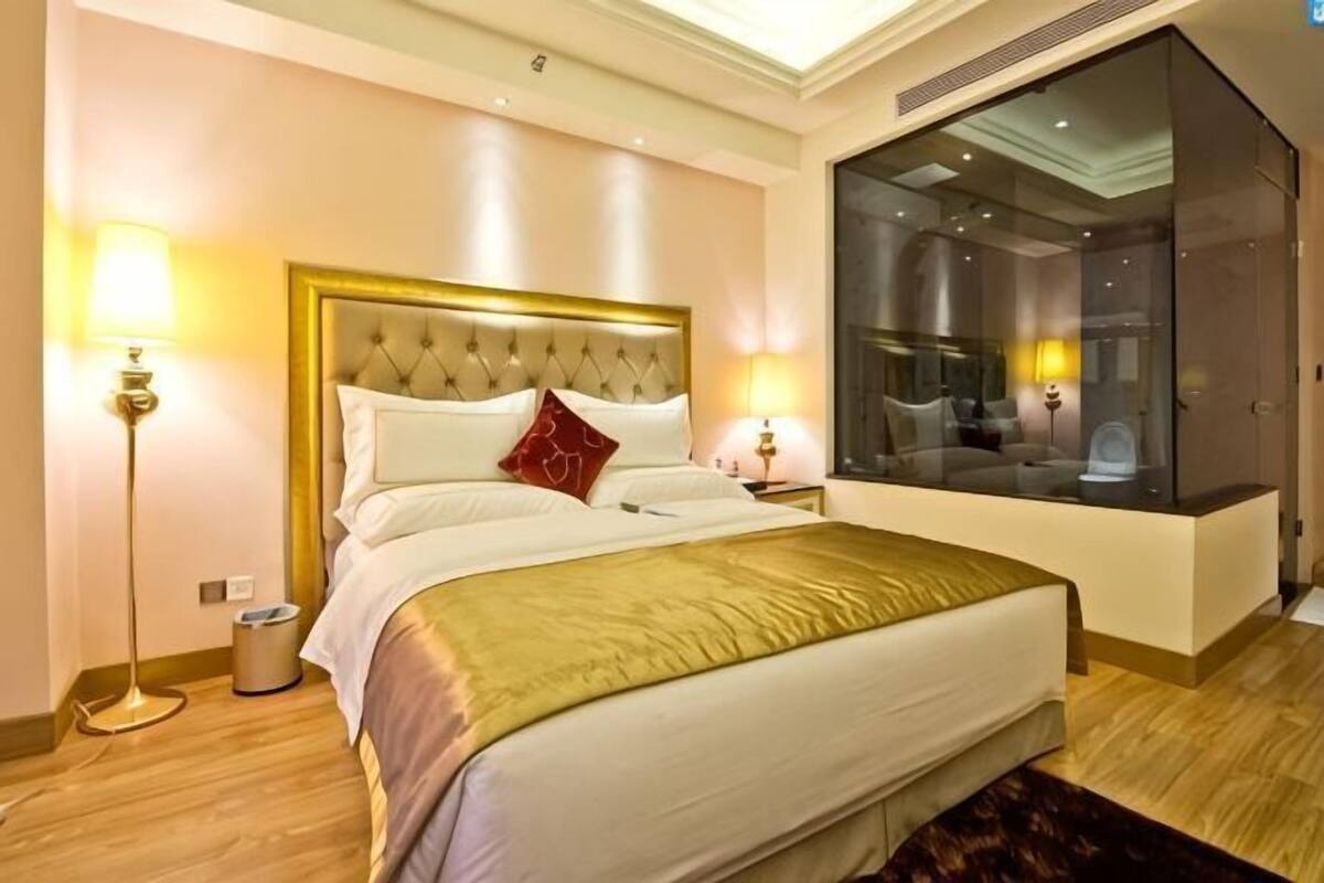 A hotel room with a large bed, bedside lamps, a modern bathroom, and a large window.
