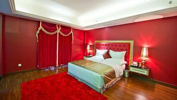 Quarto de hotel com uma cama grande, cortinas vermelhas e duas luminárias de cabeceira.