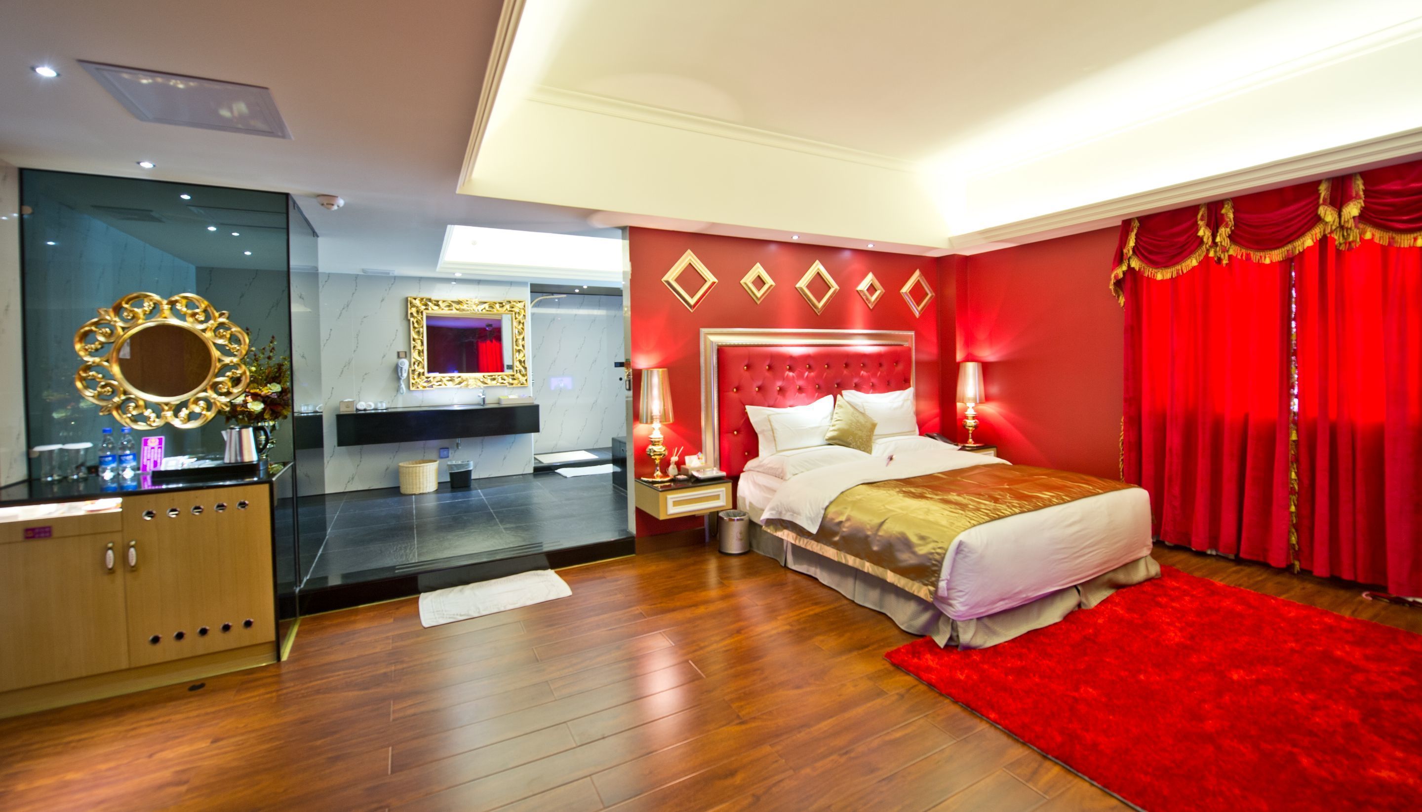 A hotel room with a bed, a vanity with a mirror, a red accent wall, and a red carpet.