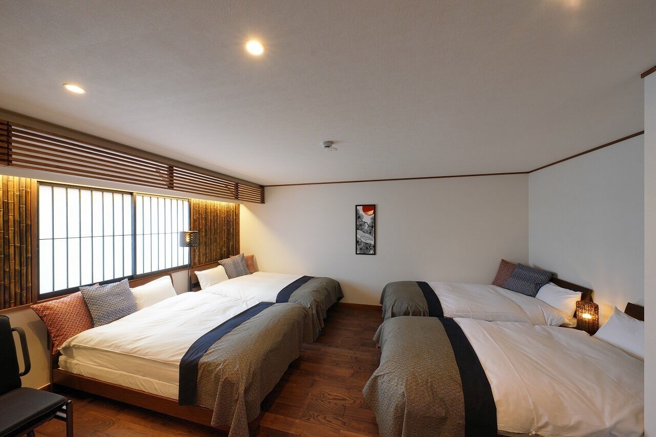 Une chambre d’hôtel avec deux lits, une fenêtre avec des stores, une œuvre d’art accrochée au mur et un luminaire au plafond.