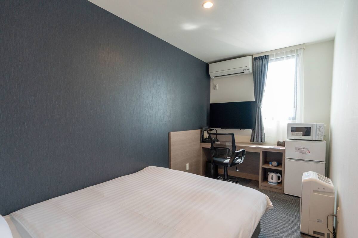A hotel room with a bed, a desk with a chair, a microwave, a coffee maker, and a TV.