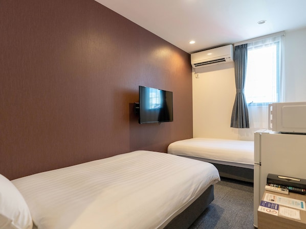 Habitación de hotel con dos camas, un televisor de pantalla plana montado en la pared, un equipo de aire acondicionado, un microondas y una ventana con cortinas.