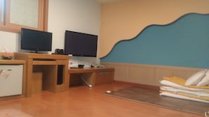 A room with a wooden desk, two televisions, a small refrigerator, and a bed with pillows. - Golden Bee Motel (Gunsan)