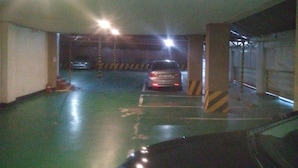 A parking garage with a car in the distance, concrete pillars, and a green floor. - Golden Bee Motel (Gunsan)