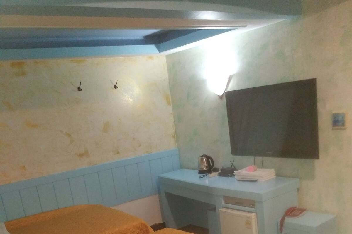 A room with two beds, a desk, a chair, a television, and a small table.