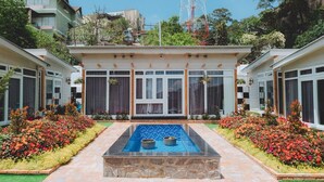 Hotel com piscina, rodeado por canteiros de flores e um caminho de pedra.