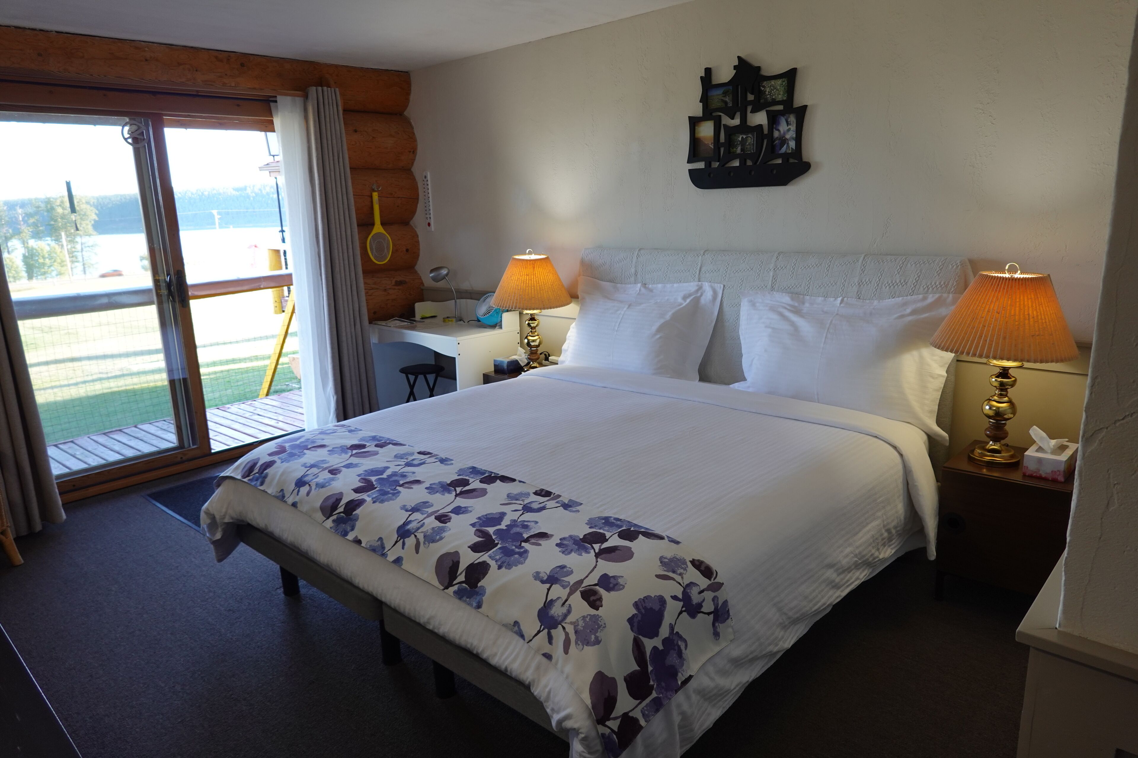 A hotel room with a large bed, two bedside lamps, a desk, and a view through a sliding glass door.