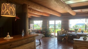A rustic wooden interior with a dining area, a sofa, and a view of the outdoors. - Cariboo Log Guest House (Lac La Hache)