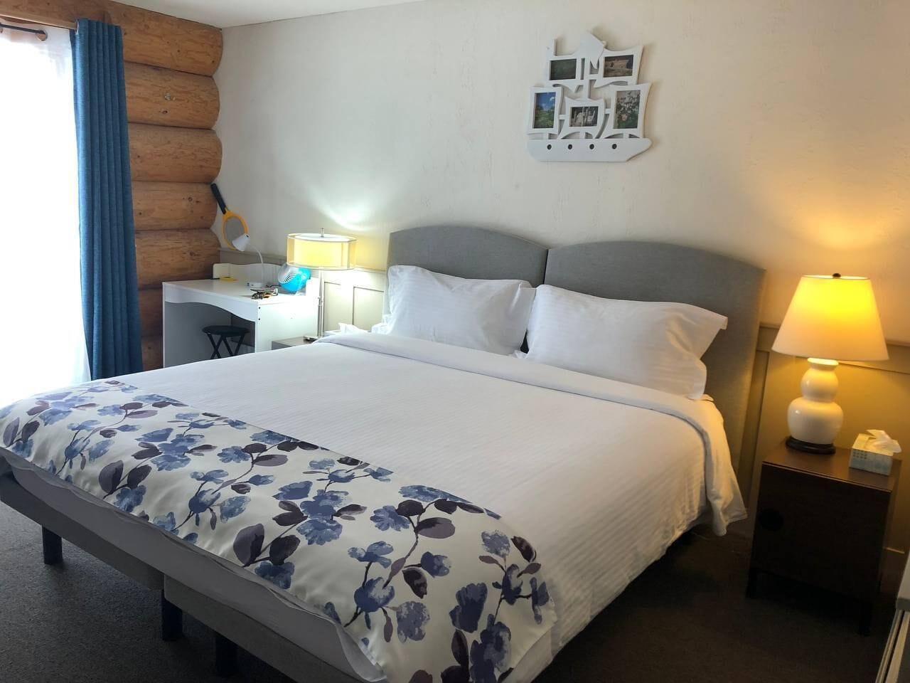 Een hotelkamer met een groot bed, een bureau en een stoel. Er staat een lamp op het bureau en een lamp op het nachtkastje.