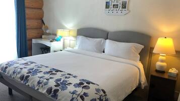 Een hotelkamer met een groot bed, een bureau en een stoel. Er staat een lamp op het bureau en een lamp op het nachtkastje.