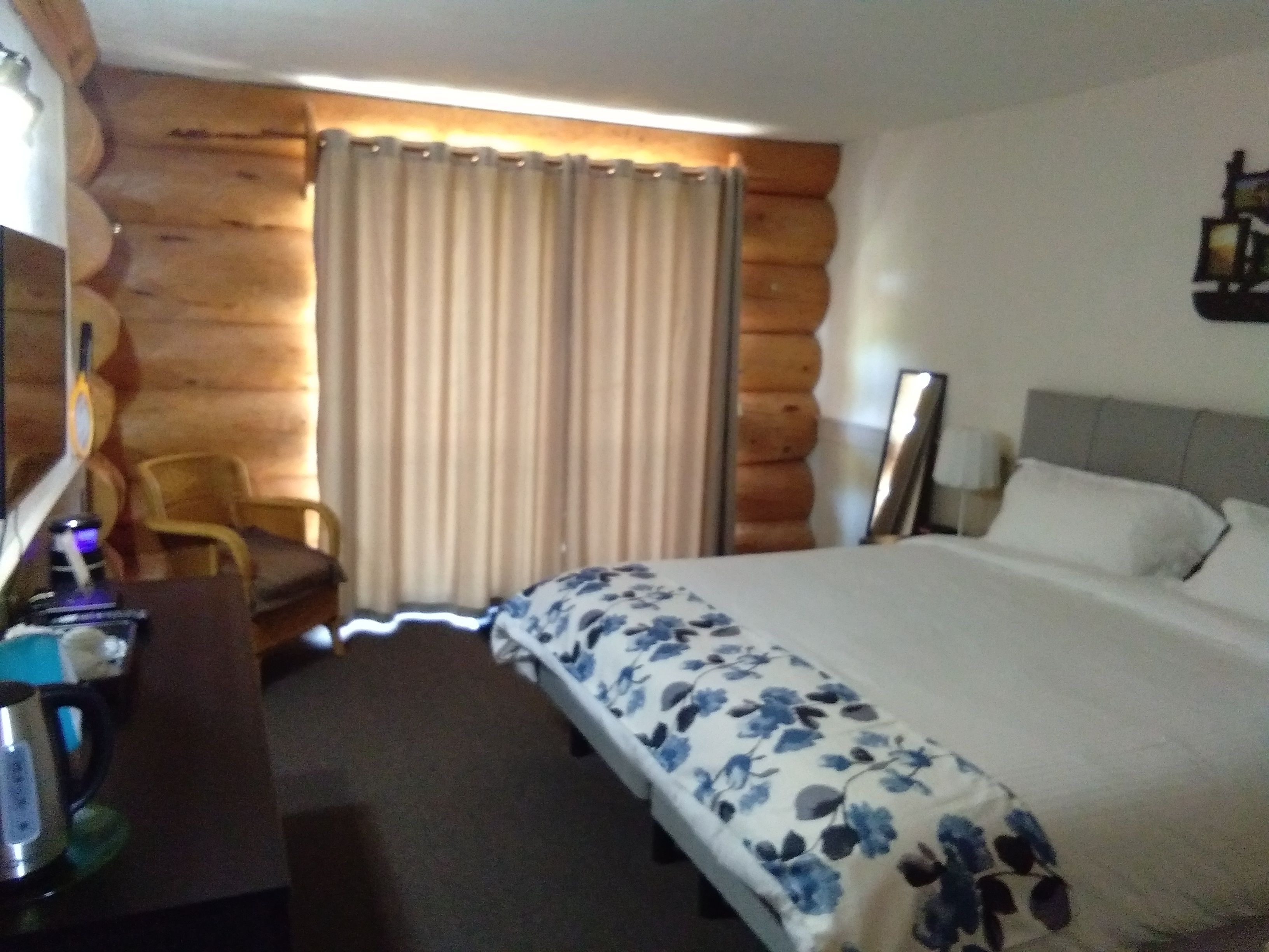 A hotel room with a bed, a desk, a chair, a mirror, and a window with curtains.